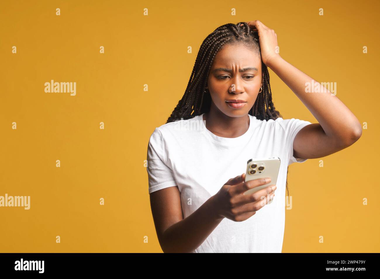 Shocked brunette young woman holding smartphone, looking at mobile phone screen and has disappointment face, received a bad news, made a mistake and a phone is locked, isolated on yellow Stock Photo
