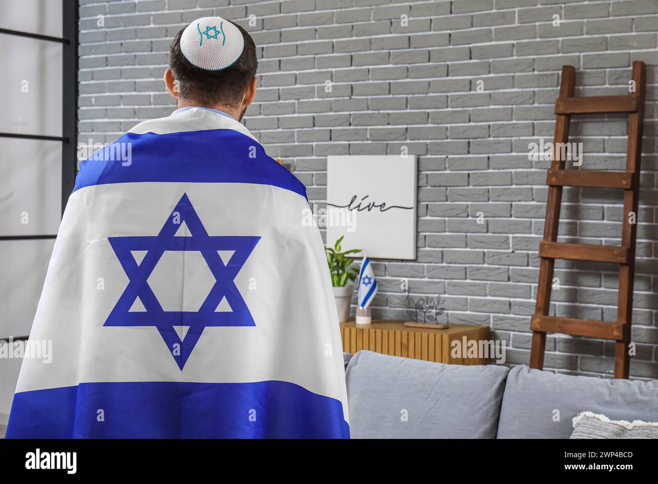 Young Jewish man in hat with flag of Israel at home, back view Stock Photo