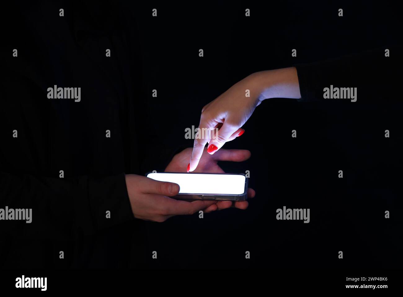 Hacker with woman using mobile phone on dark background, closeup Stock Photo