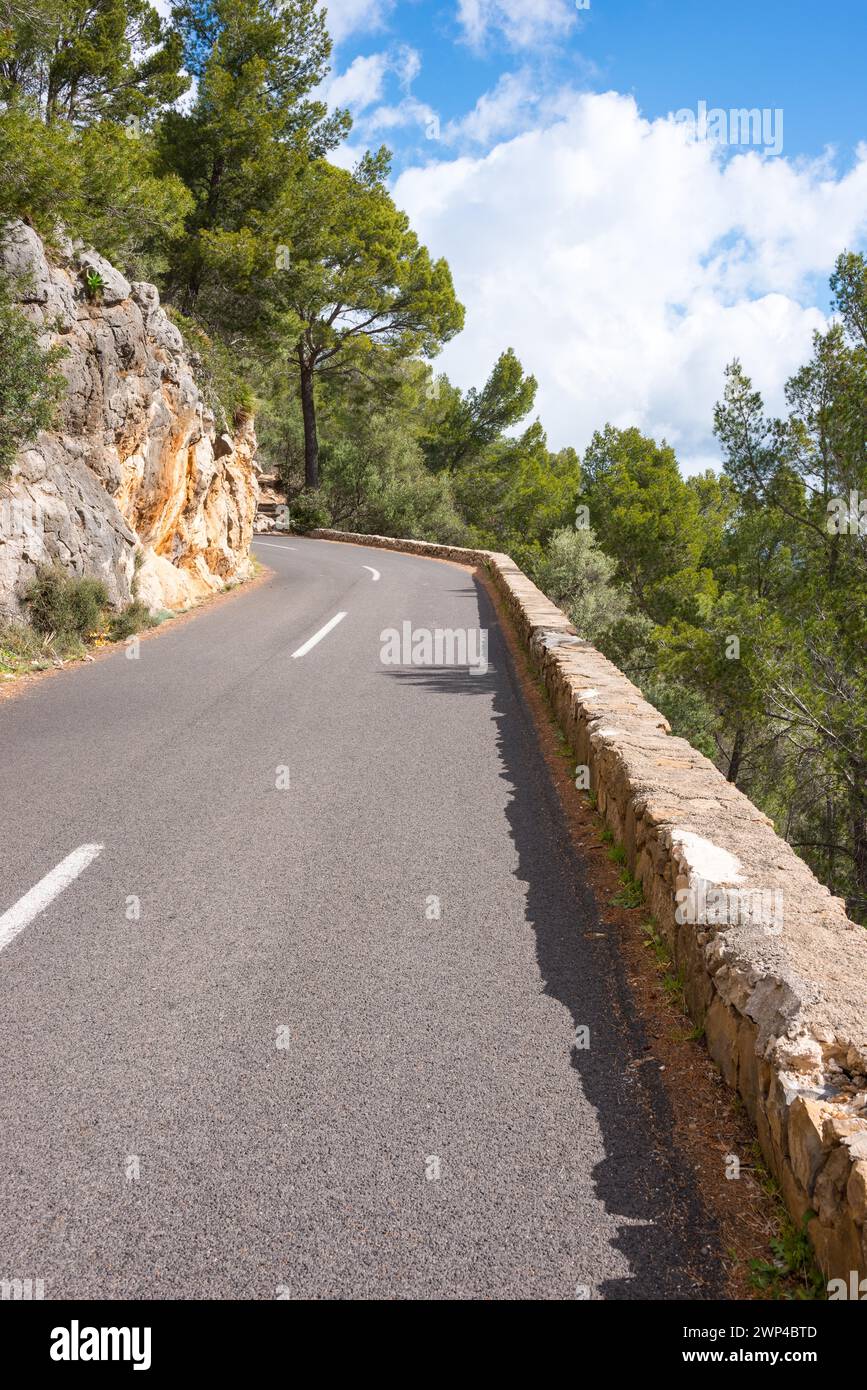 Winding, very narrow mountain road on a steep rocky slope, lined with rocks (limestone) and Mediterranean vegetation, Aleppo pines (Pinus Stock Photo