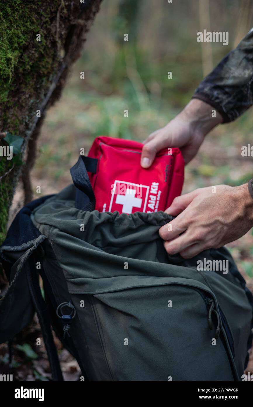 Amidst the lush wilderness of the forest, hands emerge from a hiking backpack, carefully pulling out a first aid kit. This image evokes the significan Stock Photo