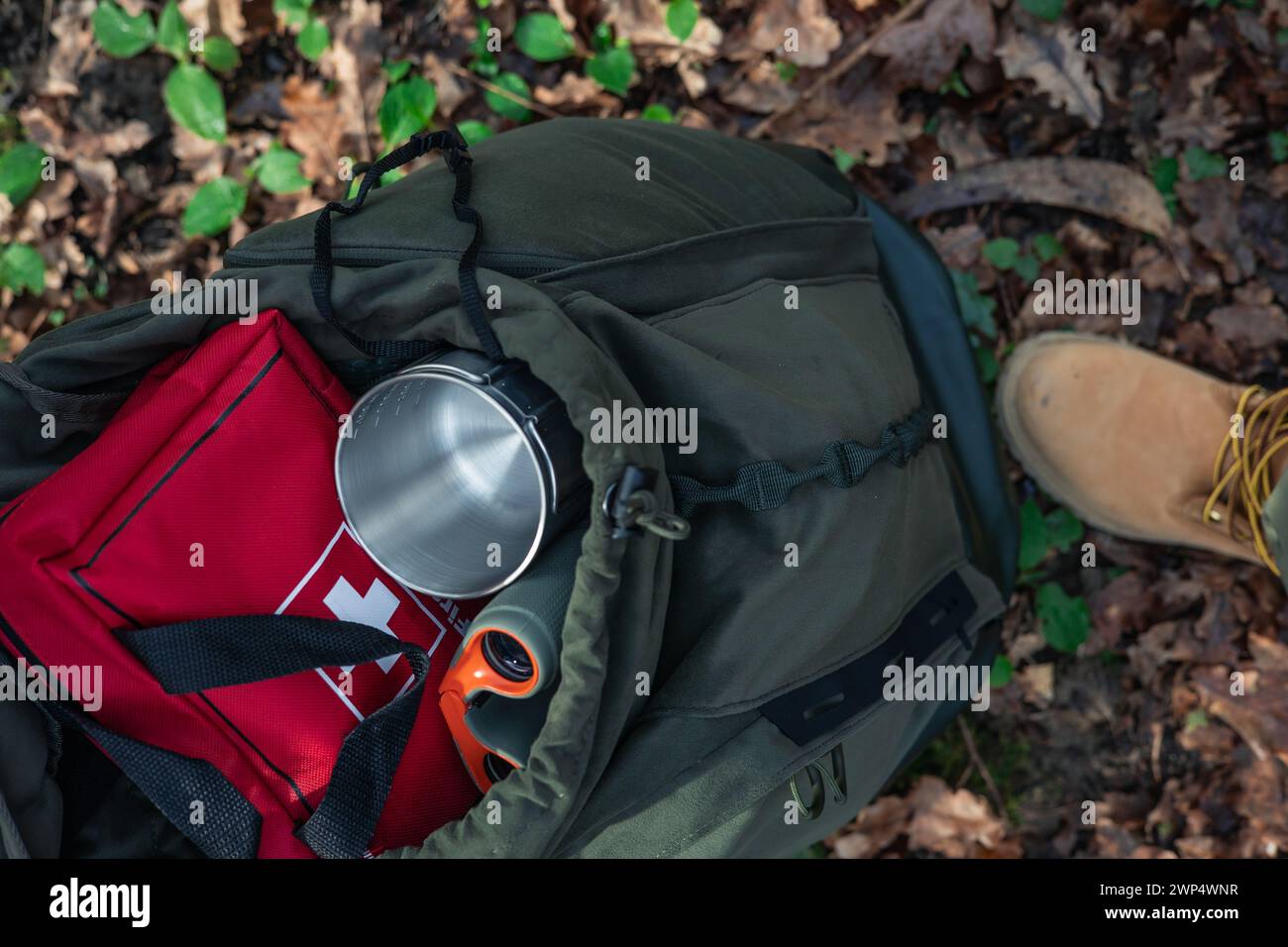 An open backpack unveils its valuable contents: a first aid kit, binoculars, and a metal cup, ready to accompany explorers on their journey through th Stock Photo