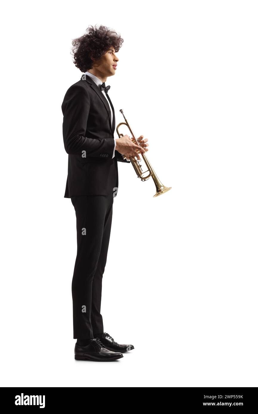 Profile shot of a young male musician in a black suit standing and holding a trumpet isolated on white background Stock Photo