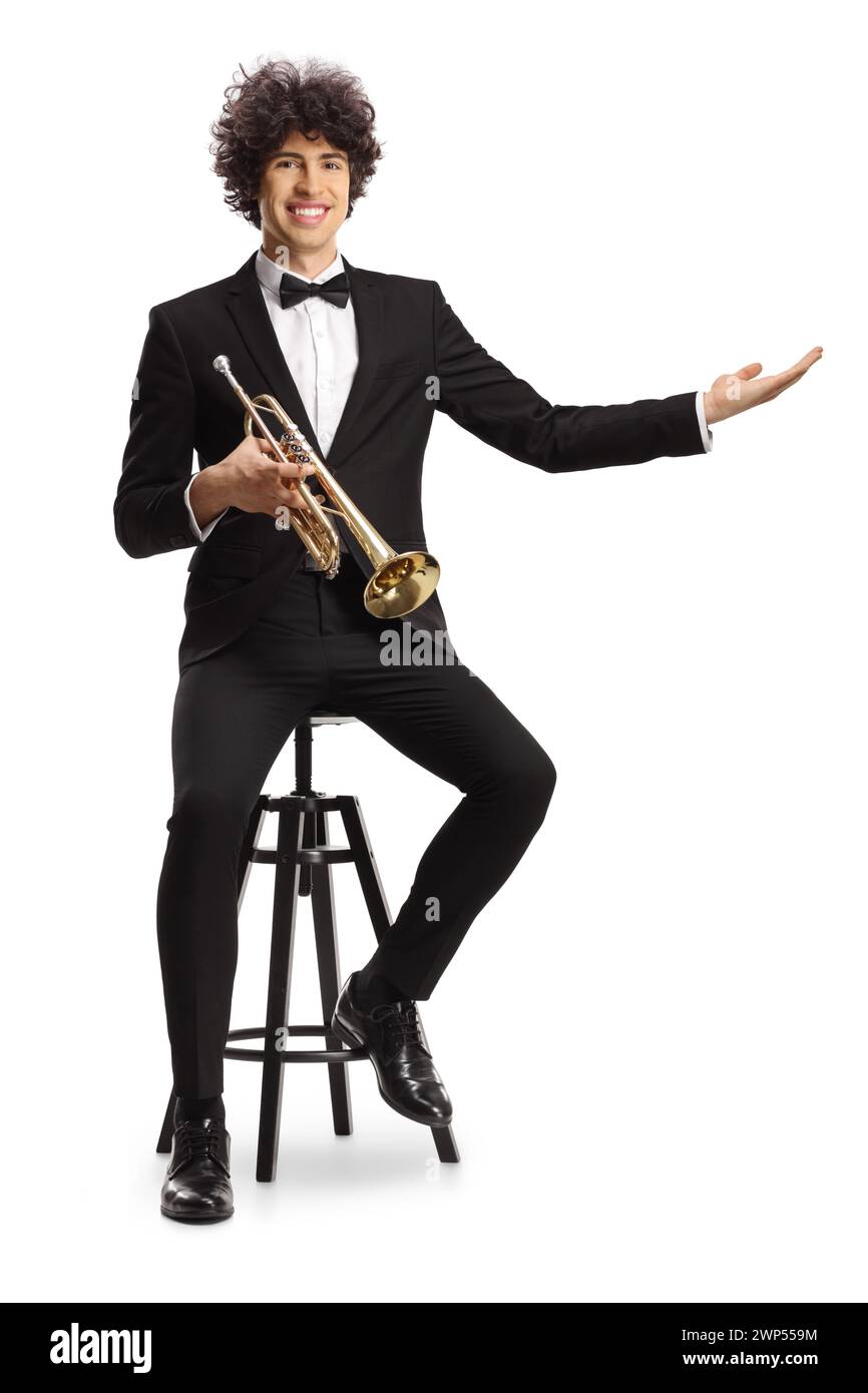 Smiling young male musician in a black suit holding a trumpet welcoming with hand isolated on white background Stock Photo