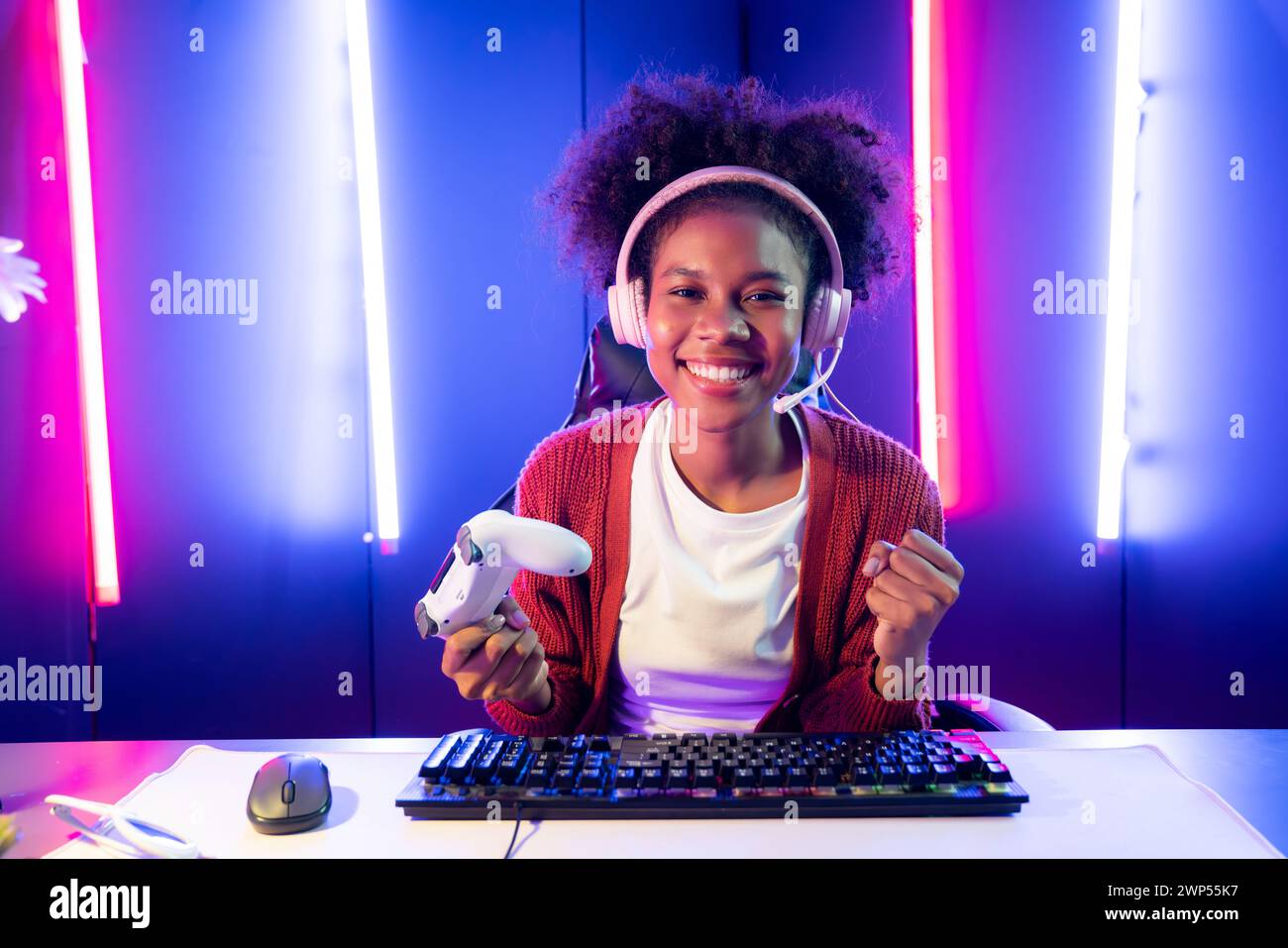 African American girl gaming streamer team winner playing online fighting with Esport wearing headphones in neon lighting room. Talking other players Stock Photo