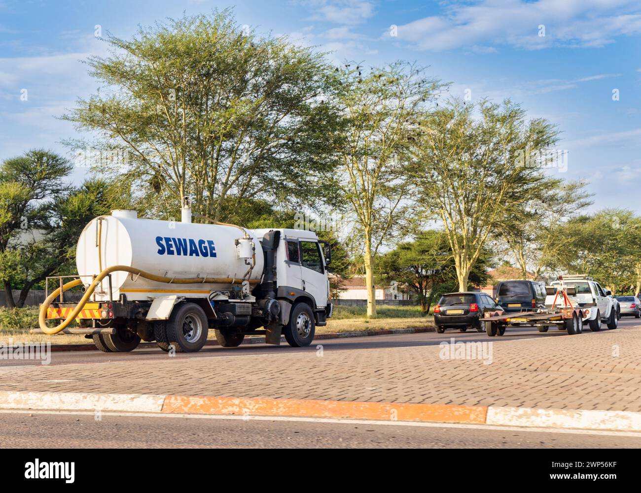 sewage truck on the road at an intersection driving behind few cars and a trailer Stock Photo