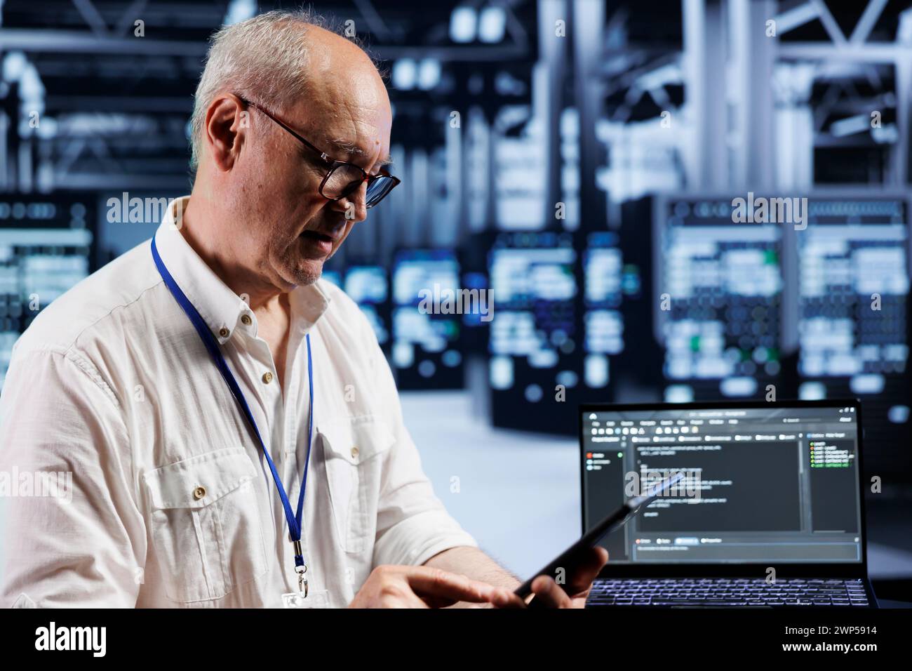Aged precise engineer coding in technologically advanced data center using javascript language. Expert updating software on server racks on laptop terminal, ensuring errorless performance and security Stock Photo
