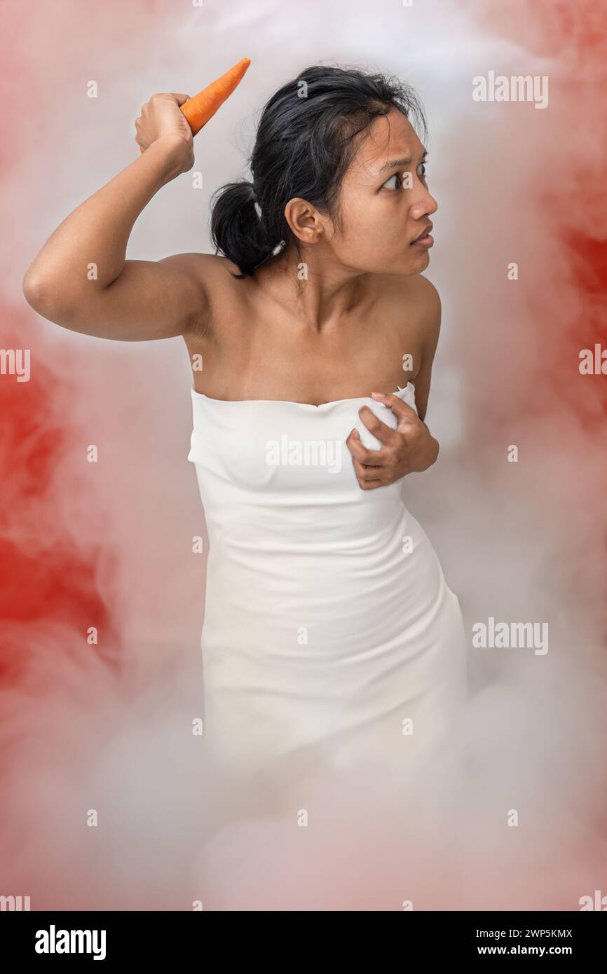 A young woman standing in white smoke is armed with a carrot Stock Photo