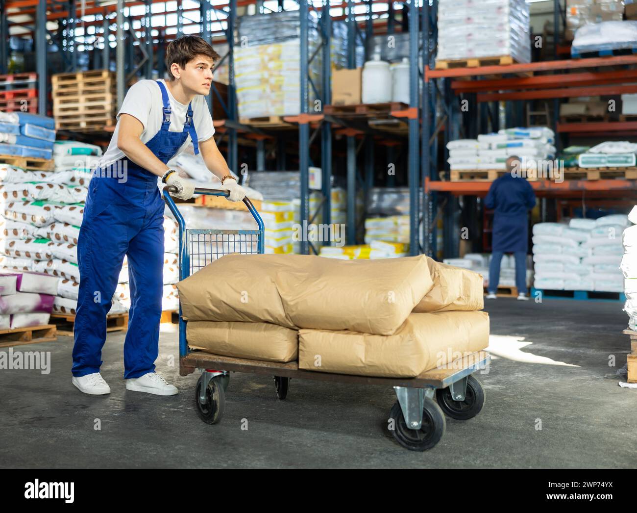 Young guy rolls cart with bags in warehouse Stock Photo
