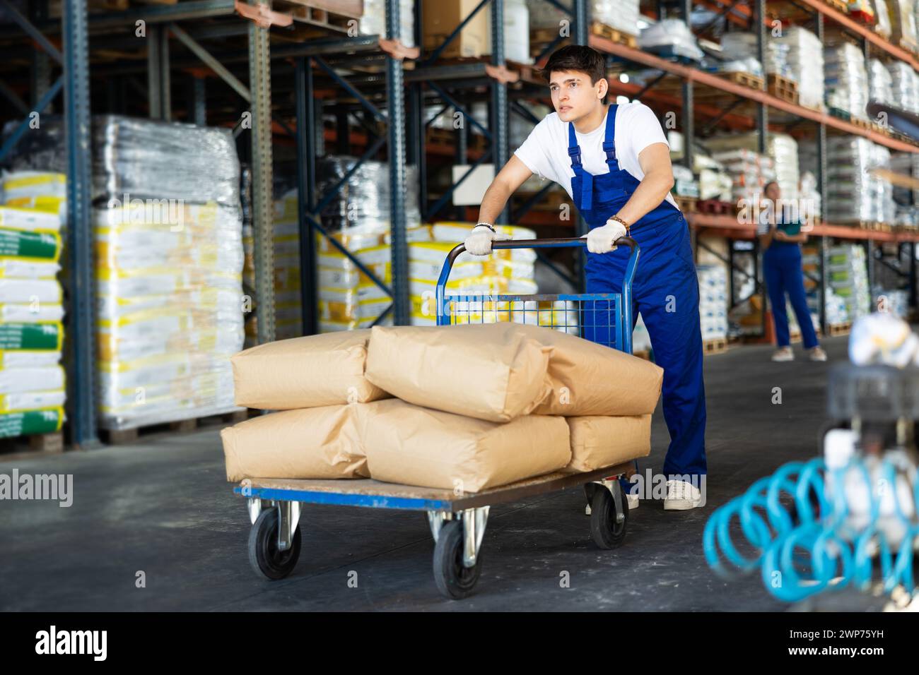 Young guy rolls cart with bags in warehouse Stock Photo