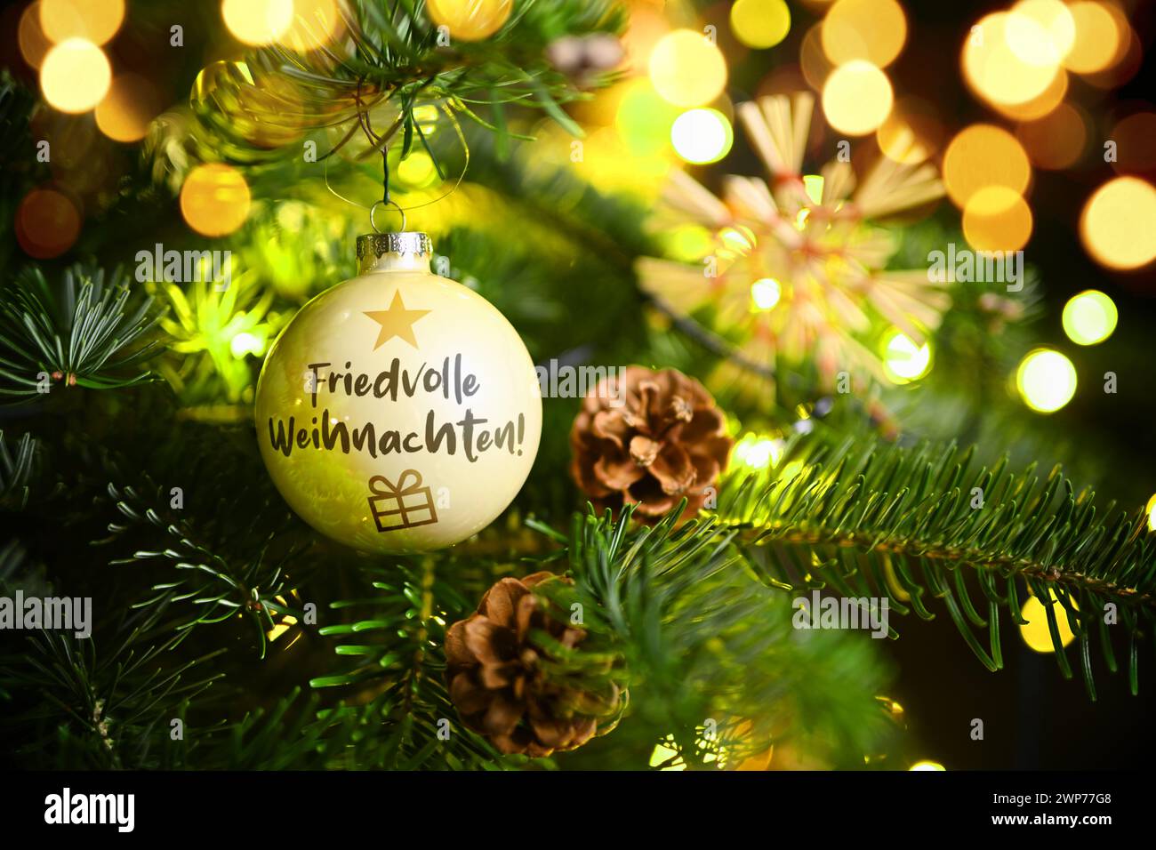 FOTOMONTAGE, Weihnachtskugel mit Aufschrift Friedvolle Weihnachten hängt an einem Weihnachtsbaum Stock Photo