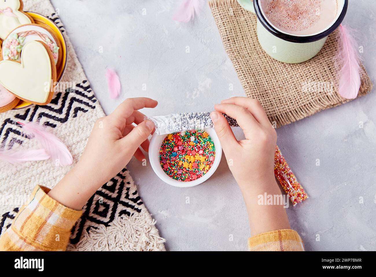 Easter joy with decorated cookies with sprinkles by child hands among sweet cocoa and pastel cookies. Stock Photo