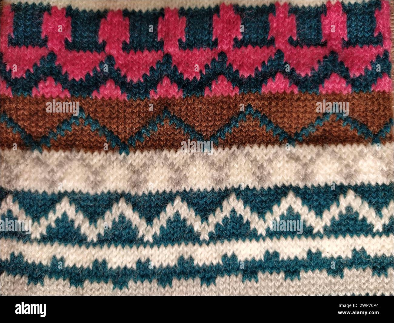 A fragment of an ornament on a knitted polyester or woolen sweater. Winter motives. Rhombuses, broken lines, waves. Knitted pattern from white, pink, Stock Photo