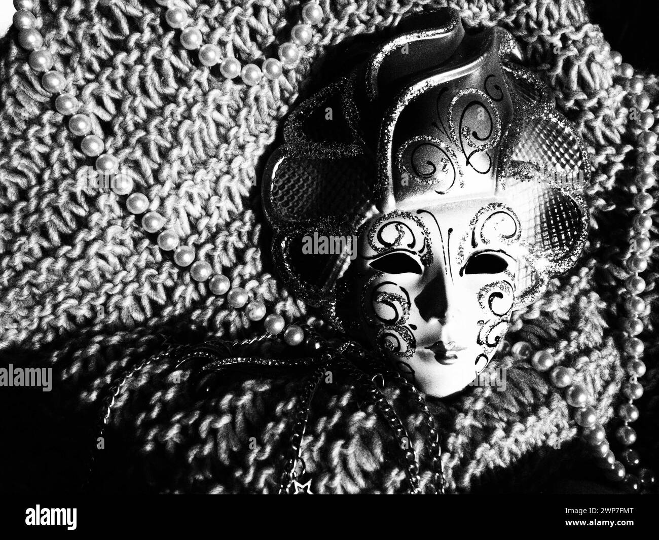 Carnival mask on a knitted background with beads and sparkles. Carnival festival costume element. Black and white monochrome image. Stock Photo