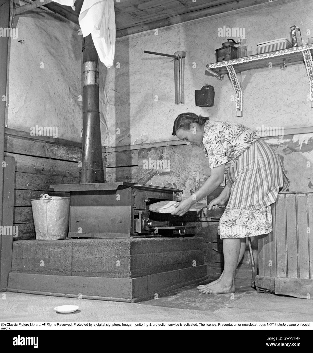 Baking bread 1949. Interior of a kitchen with a woman baking bread. A rural kitchen in Lapland Sweden 1949 with a cast-iron kitchen stove heated with firewood. Note the woman's feet, she has no socks.  Kristoffersson ref AS84-1 Stock Photo
