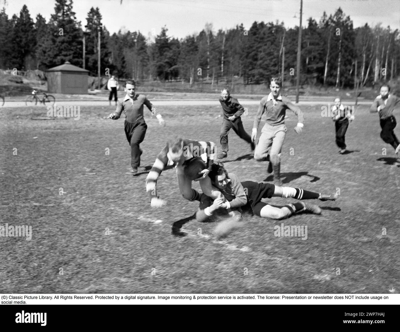 1940s rugby. A group of rugby players are practising on a sunny spring day. The player running with the rugby ball is seen being tackled and falling. Sweden May 2 1940. Kristoffersson ref 128-12 Stock Photo