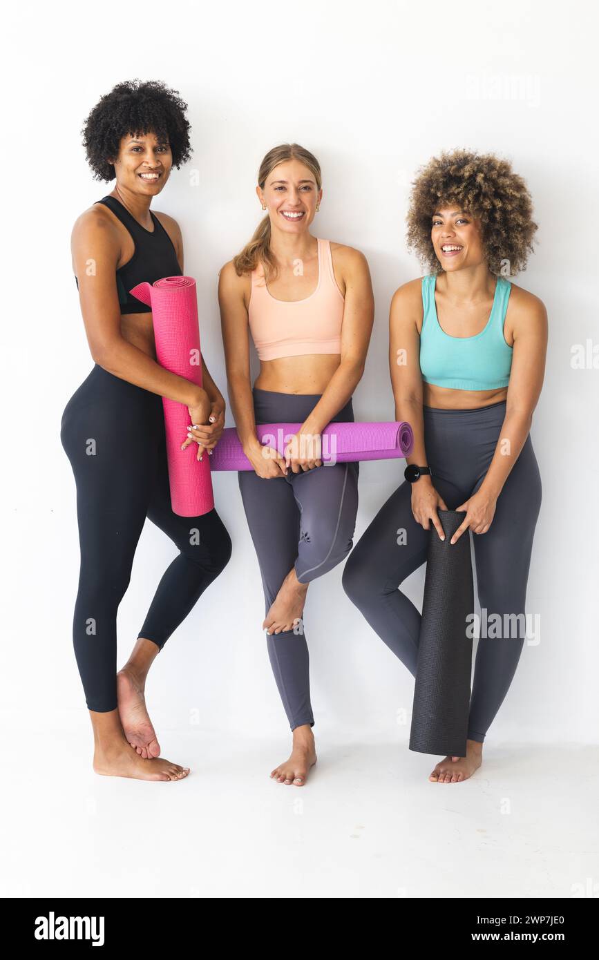 Three women pose with yoga mats, smiling in a bright studio Stock Photo