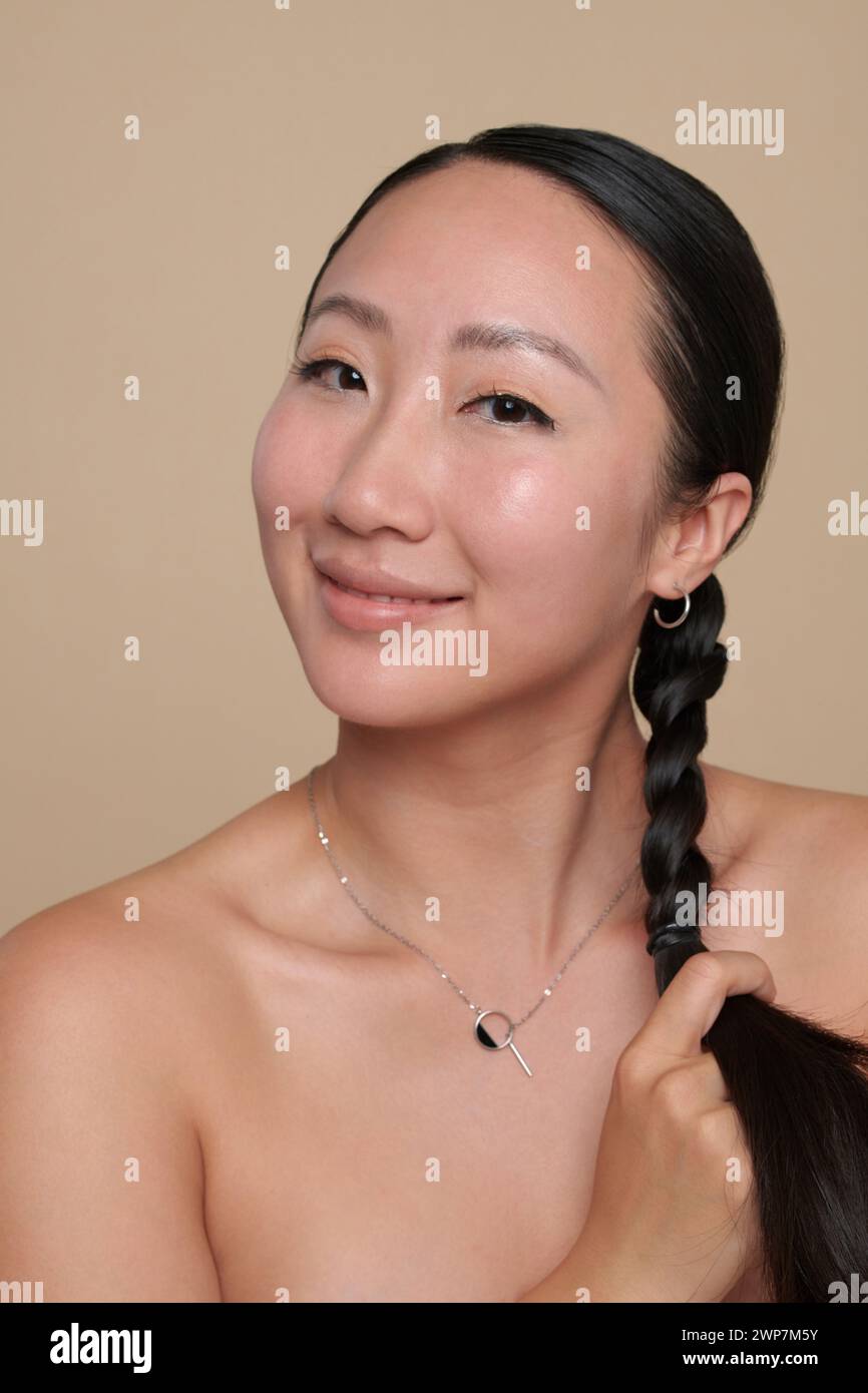 Portrait of positive Chinese woman braiding hair before going to bed