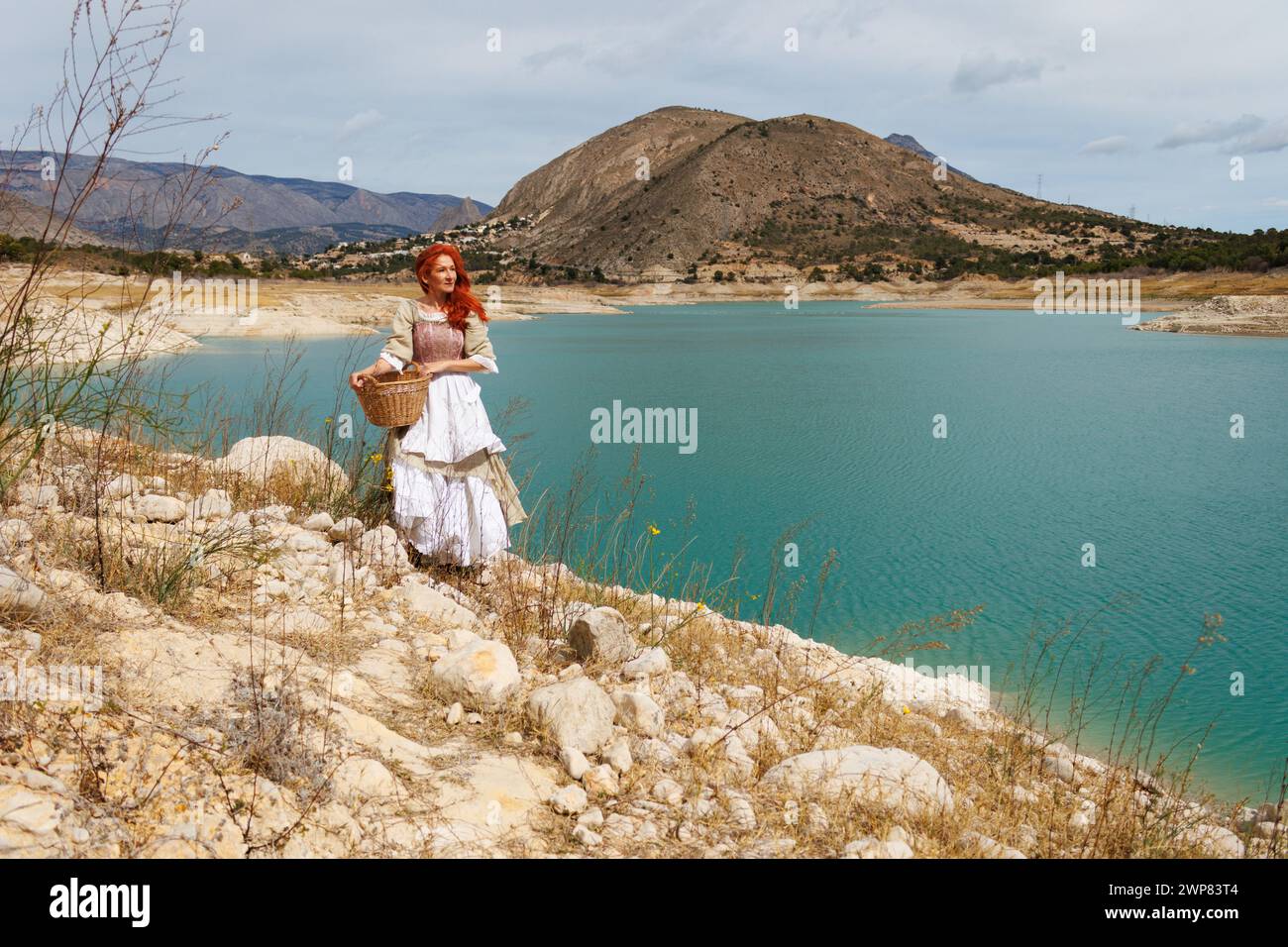Portrait of a woman dressed as a vintage peasant with the landscape of the Amador reservoir with low water levels due to climate change, Spain Stock Photo