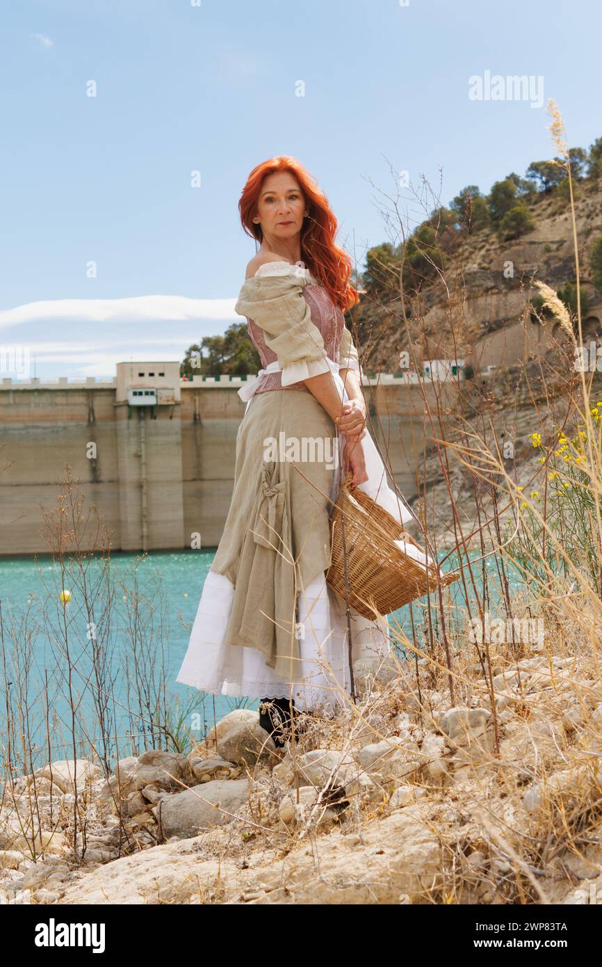 Portrait of a woman dressed as a vintage peasant with the dam of the Amadorio reservoir with low water level due to climate change, Spain Stock Photo