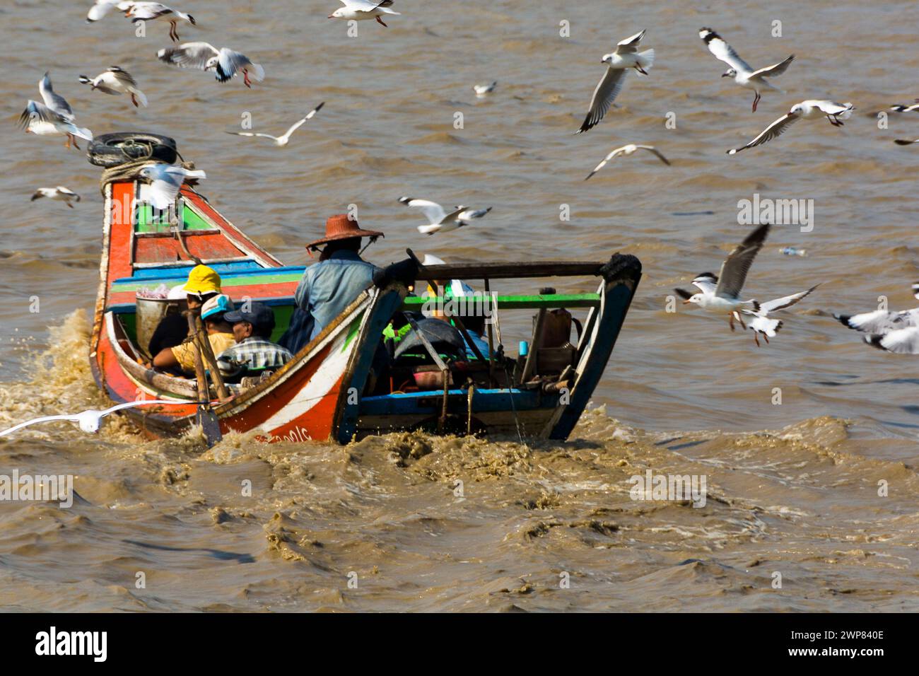 An aged fishing vessel with passengers in the sea surrounded by seabirds in Yangoon, Myanmar. Stock Photo