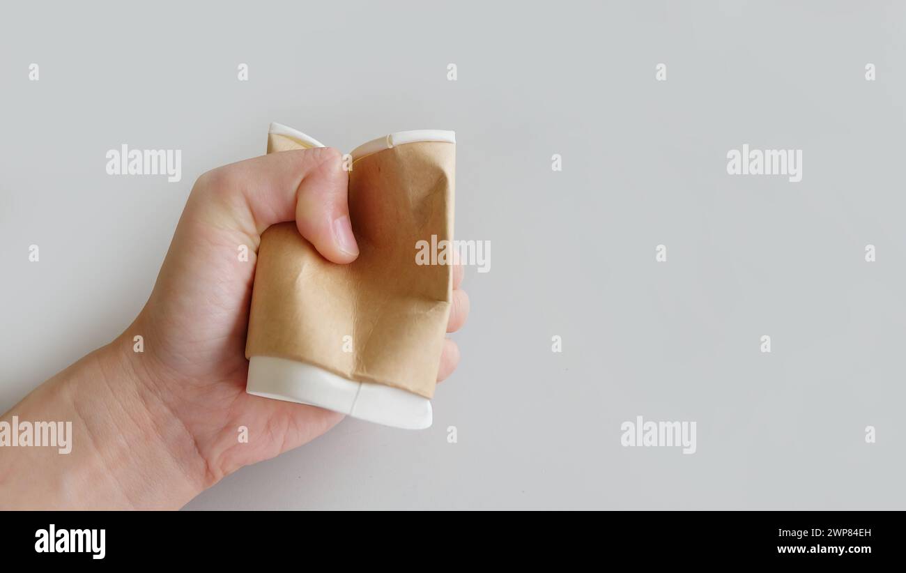 Hand holding and crushing a brown disposable paper cup Stock Photo - Alamy