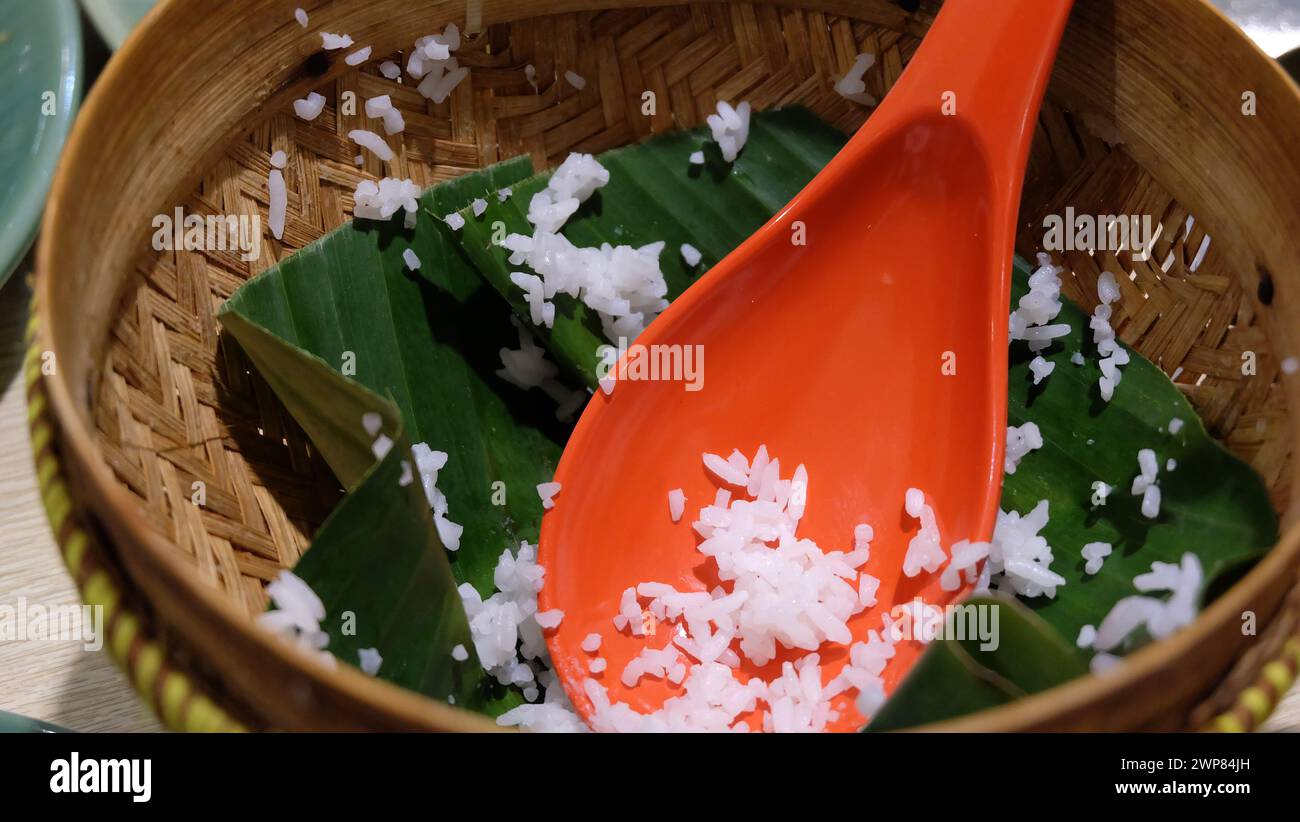 An empty serving basket with banana leaf and some leftover cooked white rice, with an orange rice ladle. Stock Photo