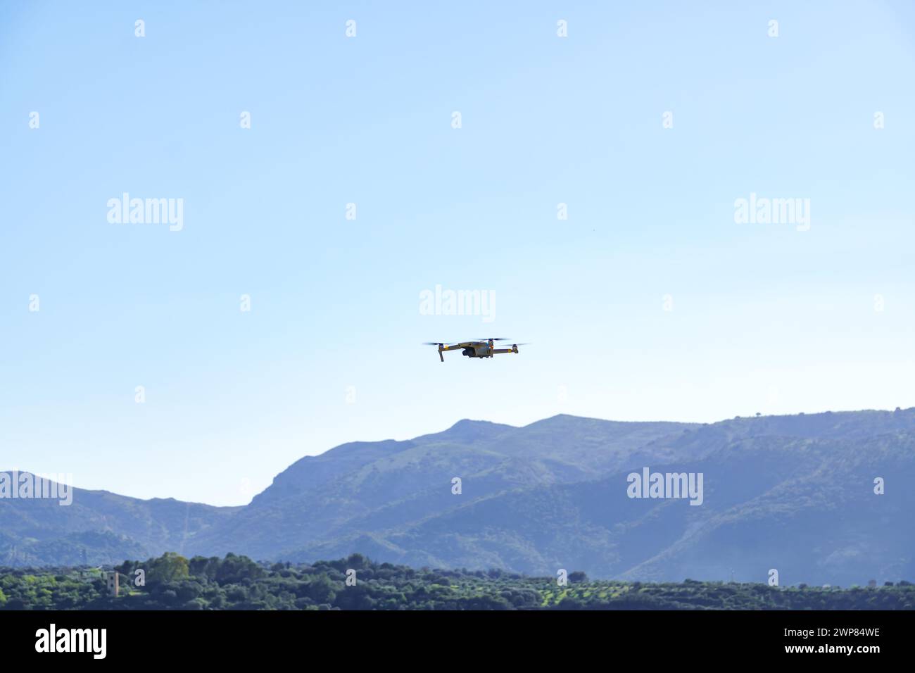 drone in flight recording a green mountain landscape with a blue sky Stock Photo