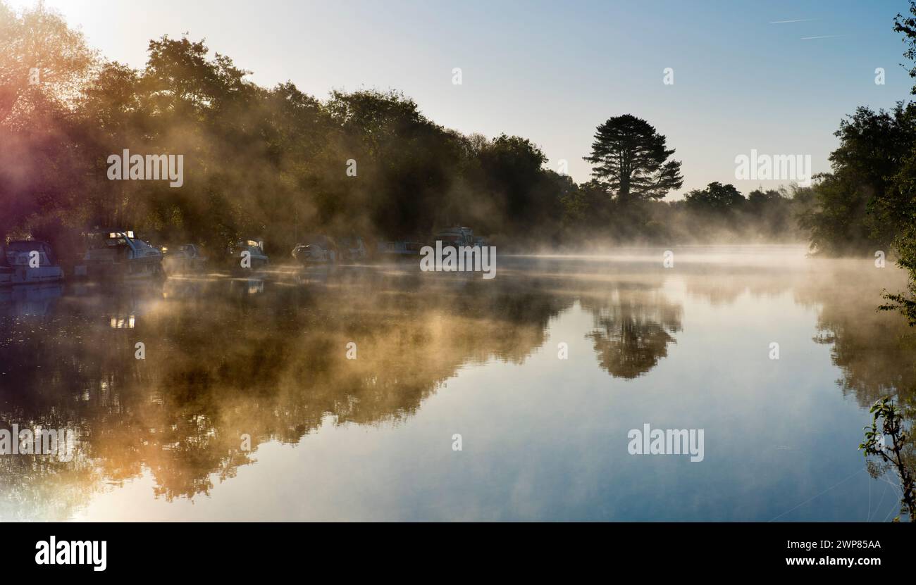 Here we see a line of pleasure boats moored by the Thames at Kennington, amidst lovely scenery just outside Oxford. It's a misty winter sunrise. Seen Stock Photo