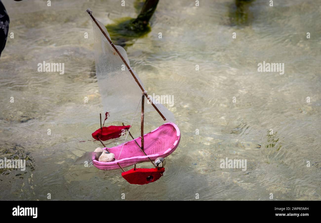 Young boy plays with toy sailing dhow made from plastic sandal on Jambiani beach, Zanzibar, Tanzania Stock Photo