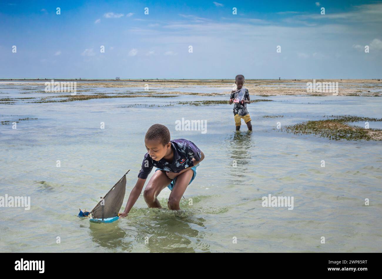 Two young boys play with toy sailing dhows made from plastic sandals on Jambiani beach, Zanzibar, Tanzania Stock Photo