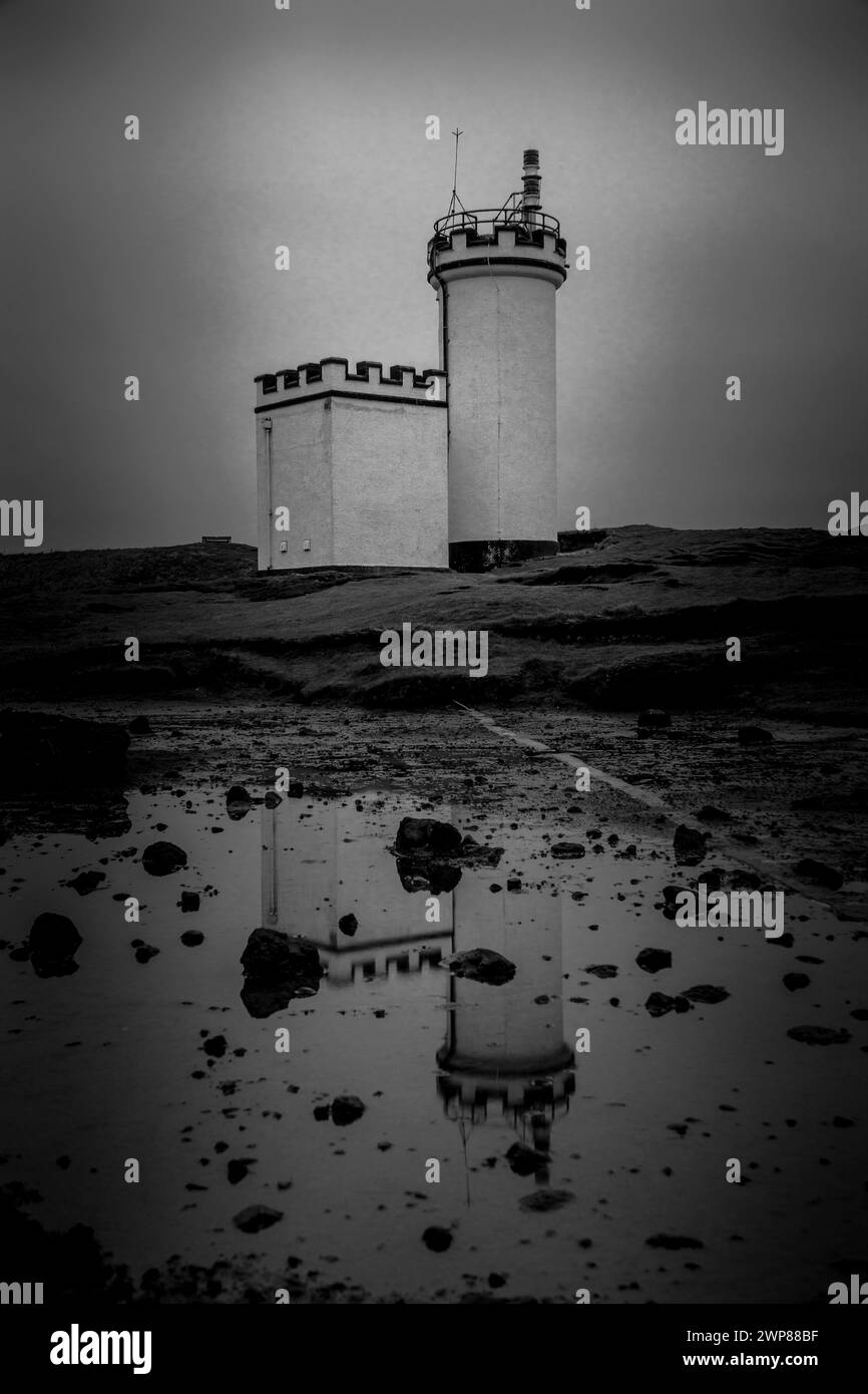 A lighthouse perched on cliff overlooking water and rocks Stock Photo