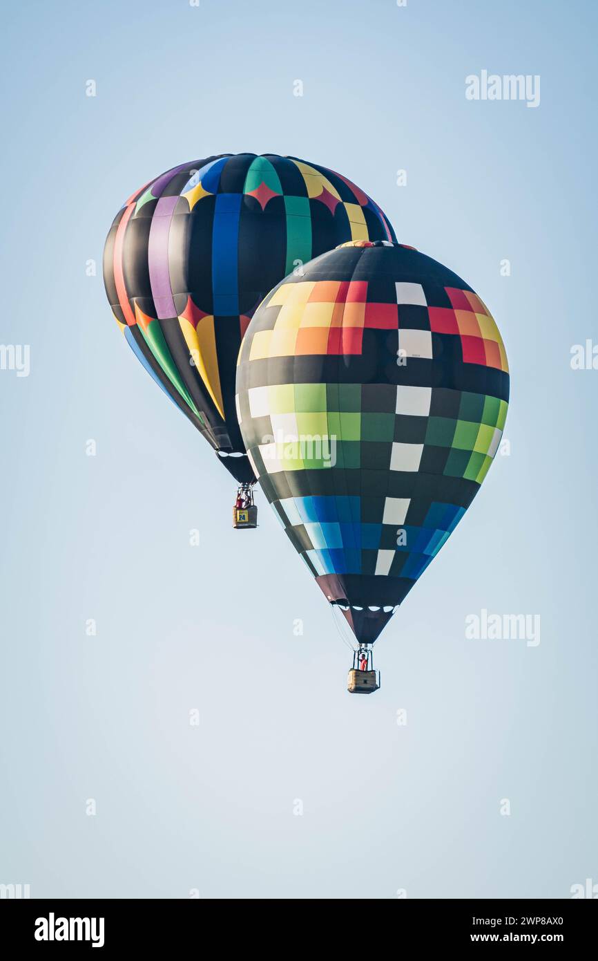 Two vibrant hot air balloons soaring together in the clear sky in Iowa