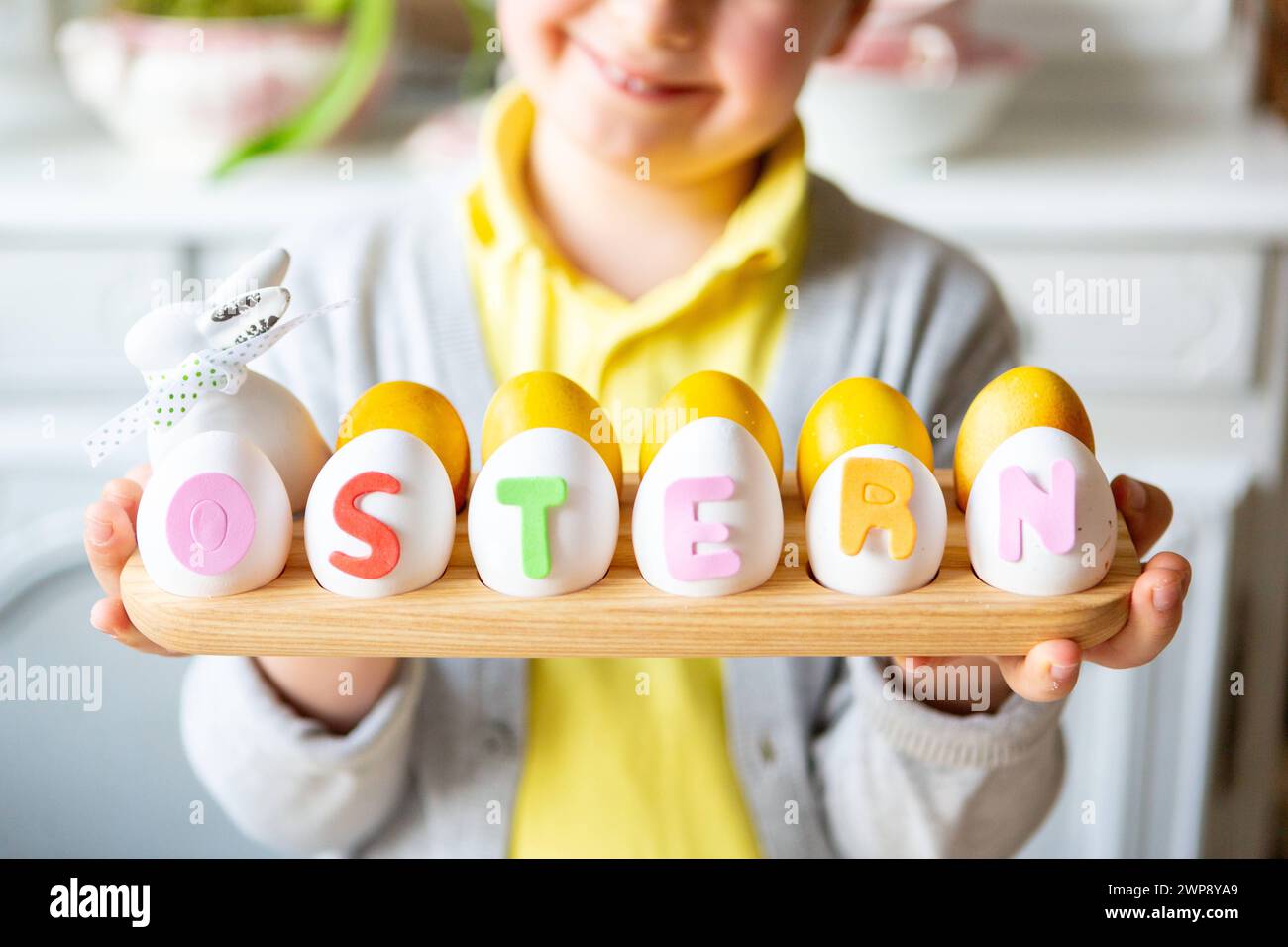 3 March 2024: Little boy making an Easter decoration. Child with bunny ears holds a handmade arrangement with eggs with the inscription: Easter *** Kleiner Junge beim Basteln einer Osterdekoration. Kind mit Hasenohren hält ein gebasteltes Gesteck mit Eiern mit der Aufschrift: Ostern Stock Photo