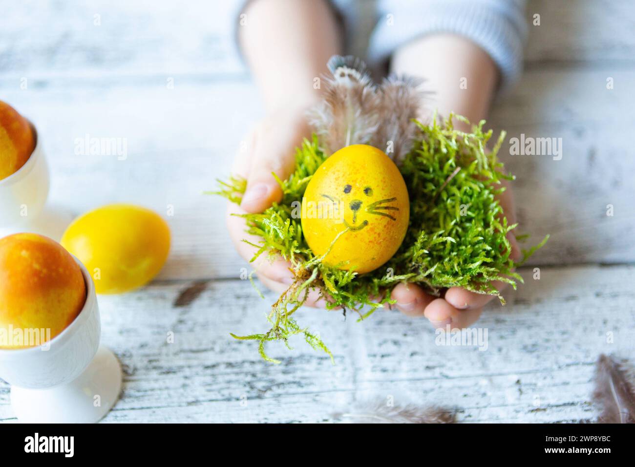3 March 2024: Child holding a self-made Easter egg with bunny ears and face for Easter. Easter nest *** Kind hält ein selbstgebasteltes Osterei mit Hasenohren und Gesicht zu Ostern. Osternest Stock Photo
