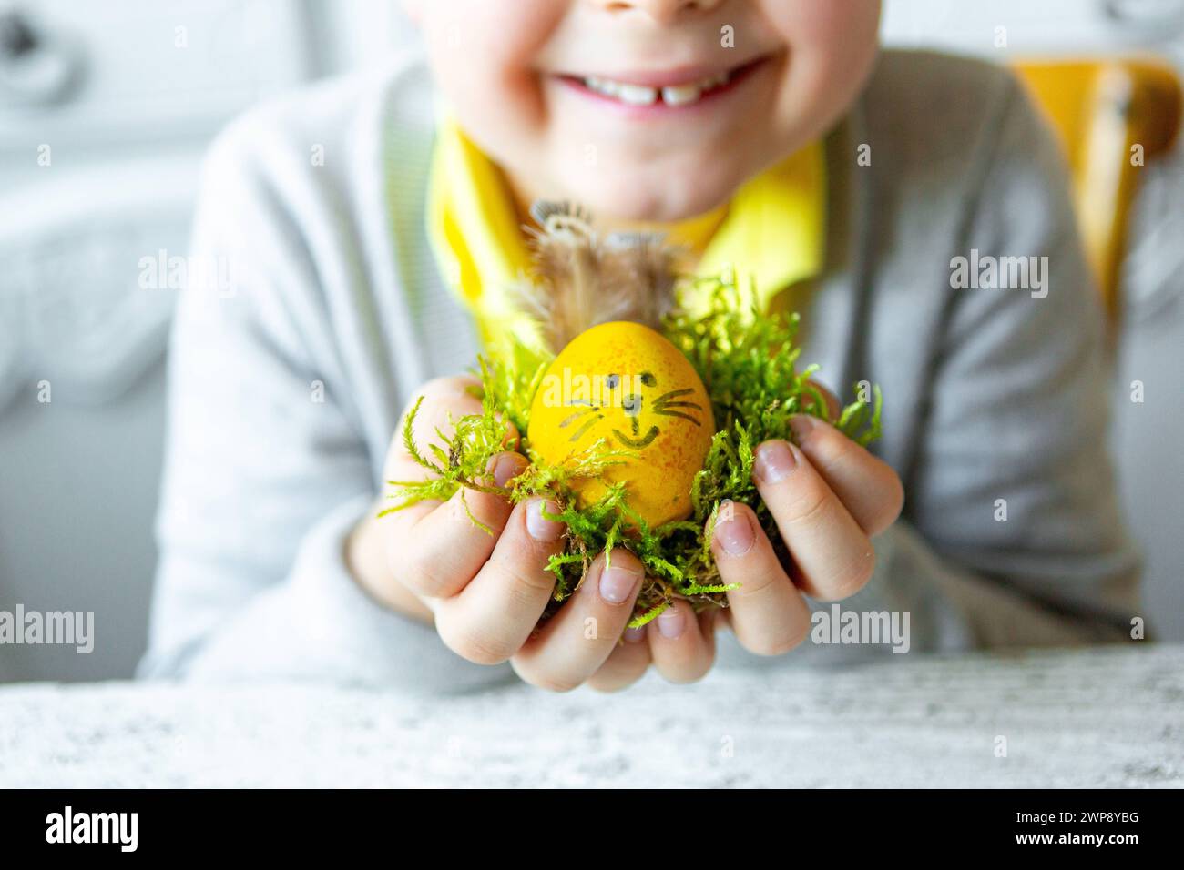 3 March 2024: Child holding a self-made Easter egg with bunny ears and face for Easter. Easter nest *** Kind hält ein selbstgebasteltes Osterei mit Hasenohren und Gesicht zu Ostern. Osternest Stock Photo