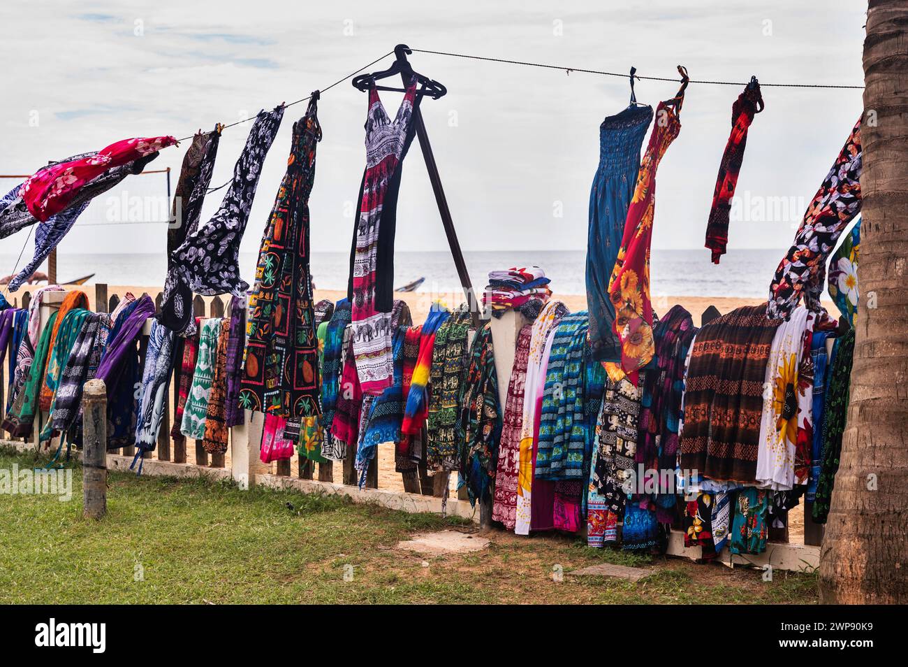 Many colorful dresses, scarf and skirts hang on cord and flies in wind on beach. Sri Lanka, Waskaduwa. Stock Photo