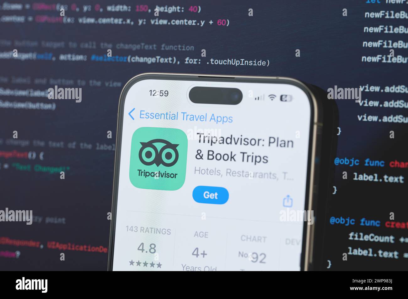 New York, USA - February 23, 2024: Tripadvisor on iphone screen in blurred code programming background Stock Photo