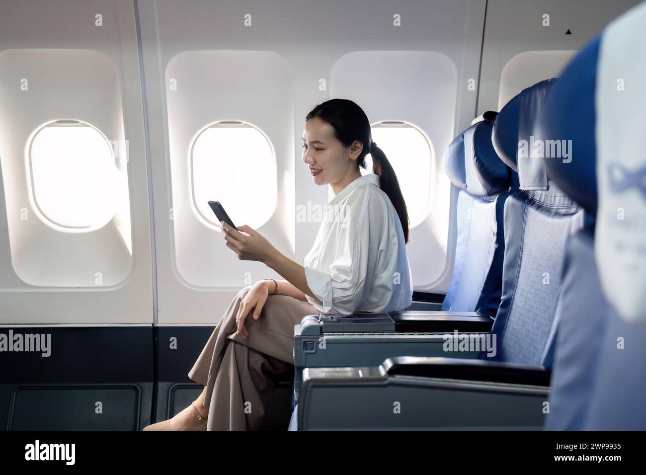 A woman is sitting on an airplane and looking at her phone Stock Photo