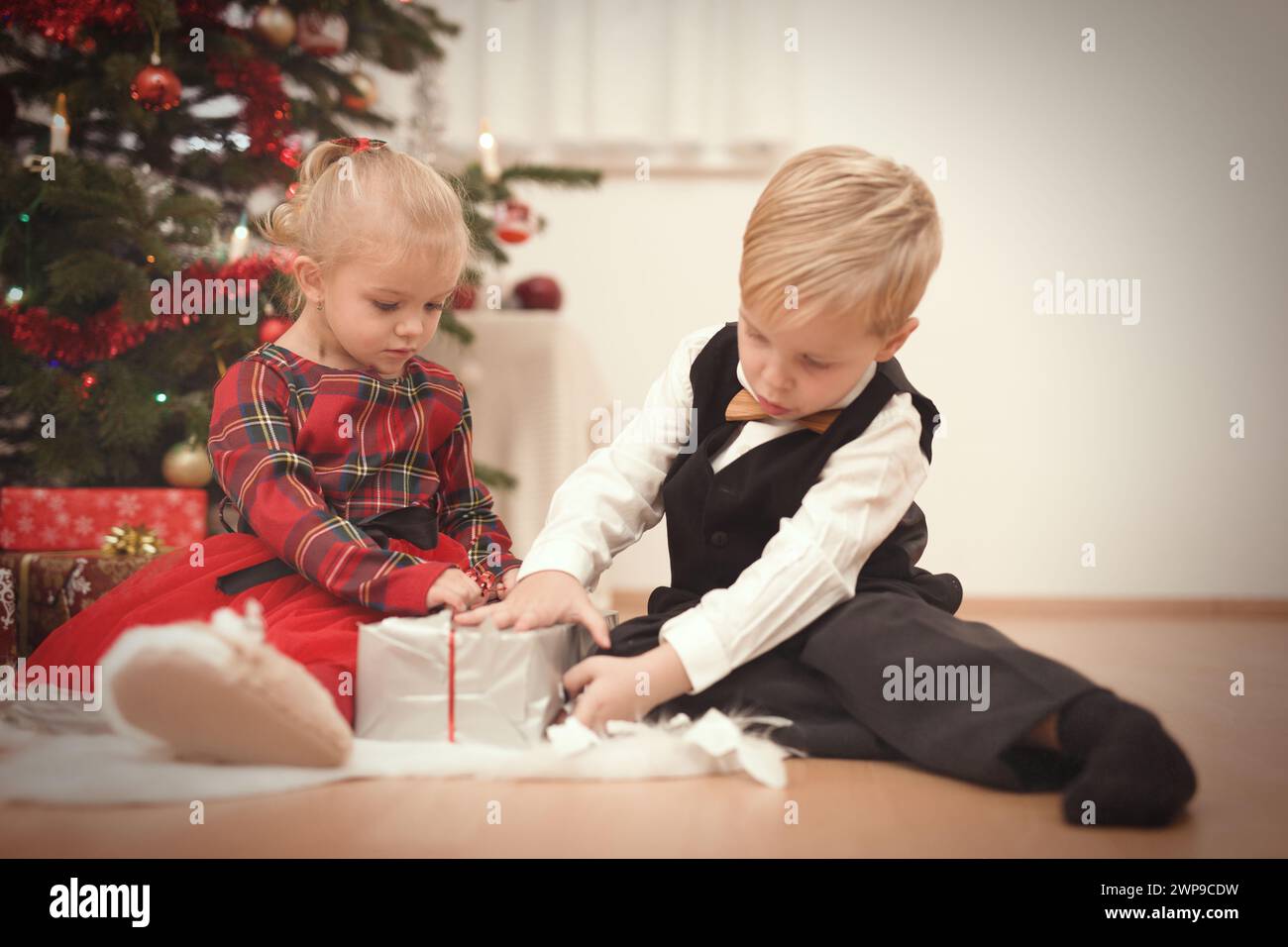 Couple of Children at time of christmas day unpacking gifts near tree Stock Photo