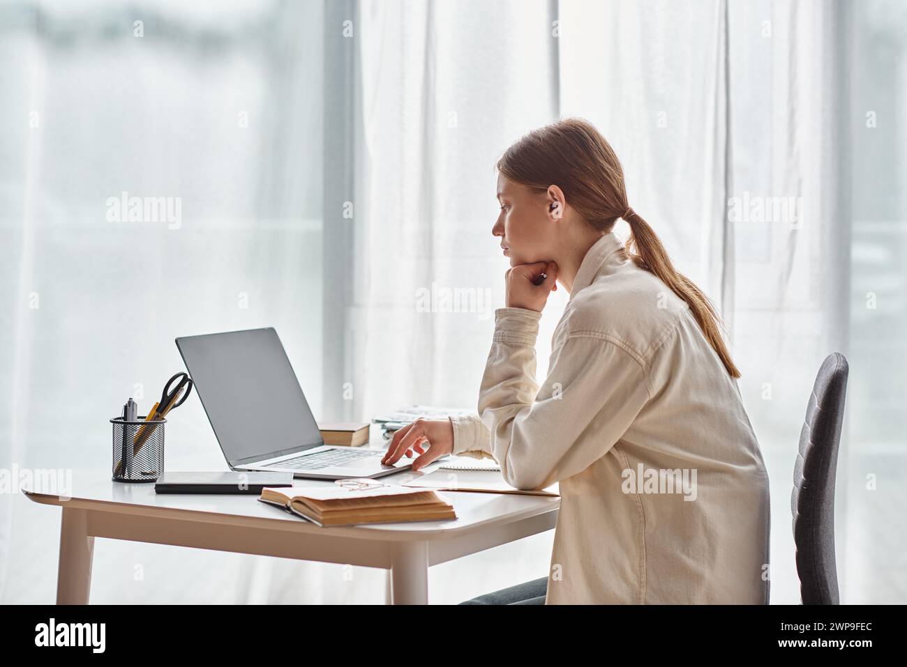 bored teenage girl using her laptop while sitting around books ...