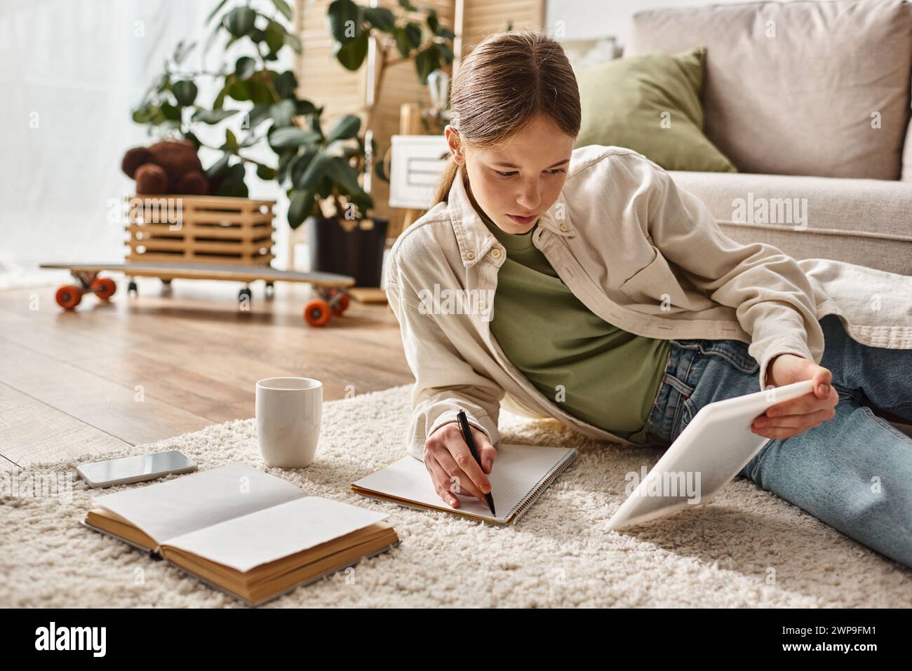 teenage girl holding tablet and taking notes while making her homework ...
