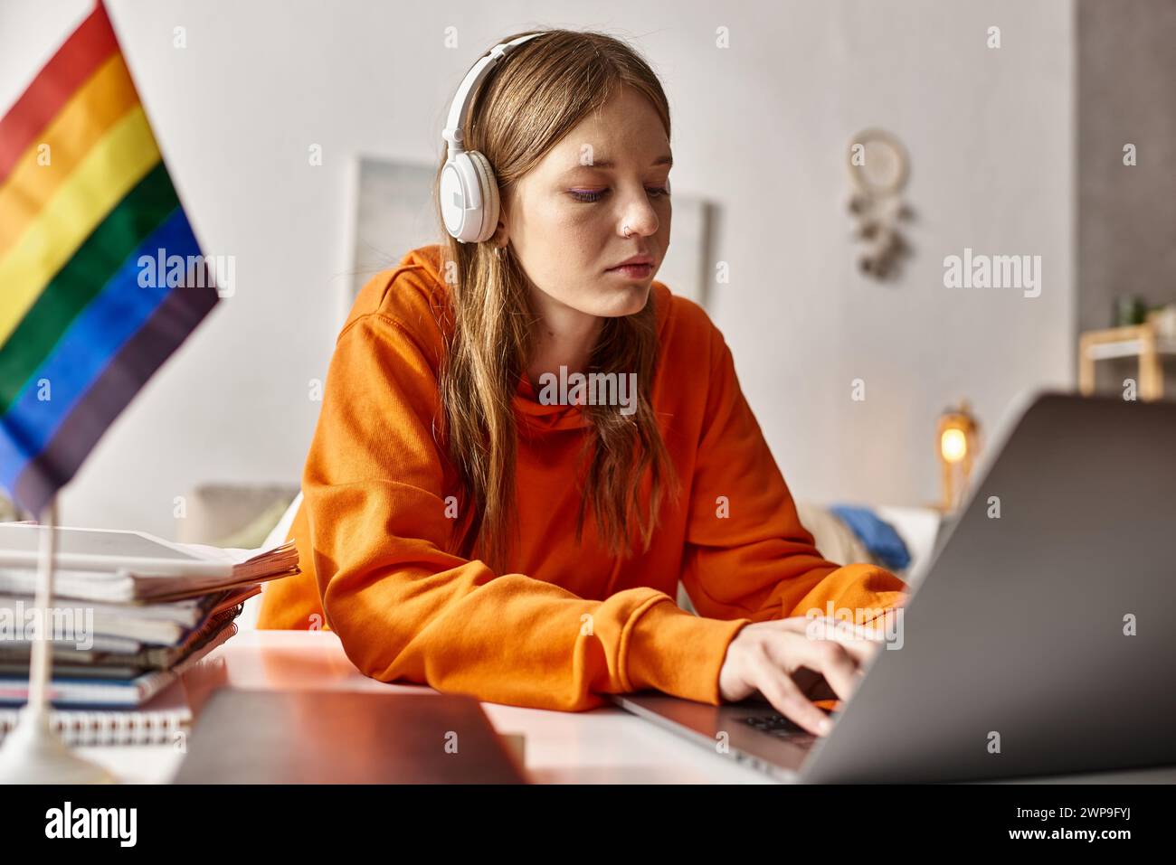 focused young teenage girl in wireless headphones typing on her laptop ...