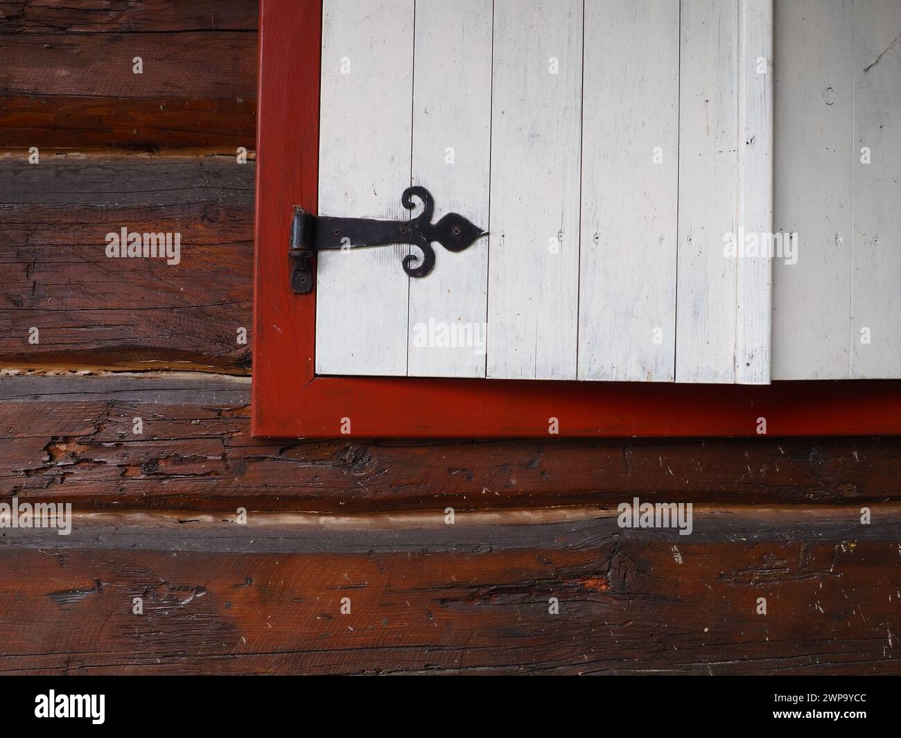 Ethno-folk wooden shutters on a window with a wooden frame, painted red and white. Metal loop bracket in the form of an arrow and a heart Stock Photo