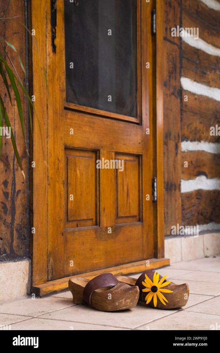 Pair of old clogs with brown leather strap in front of back entrance door on old reconstructed log cabin. Stock Photo