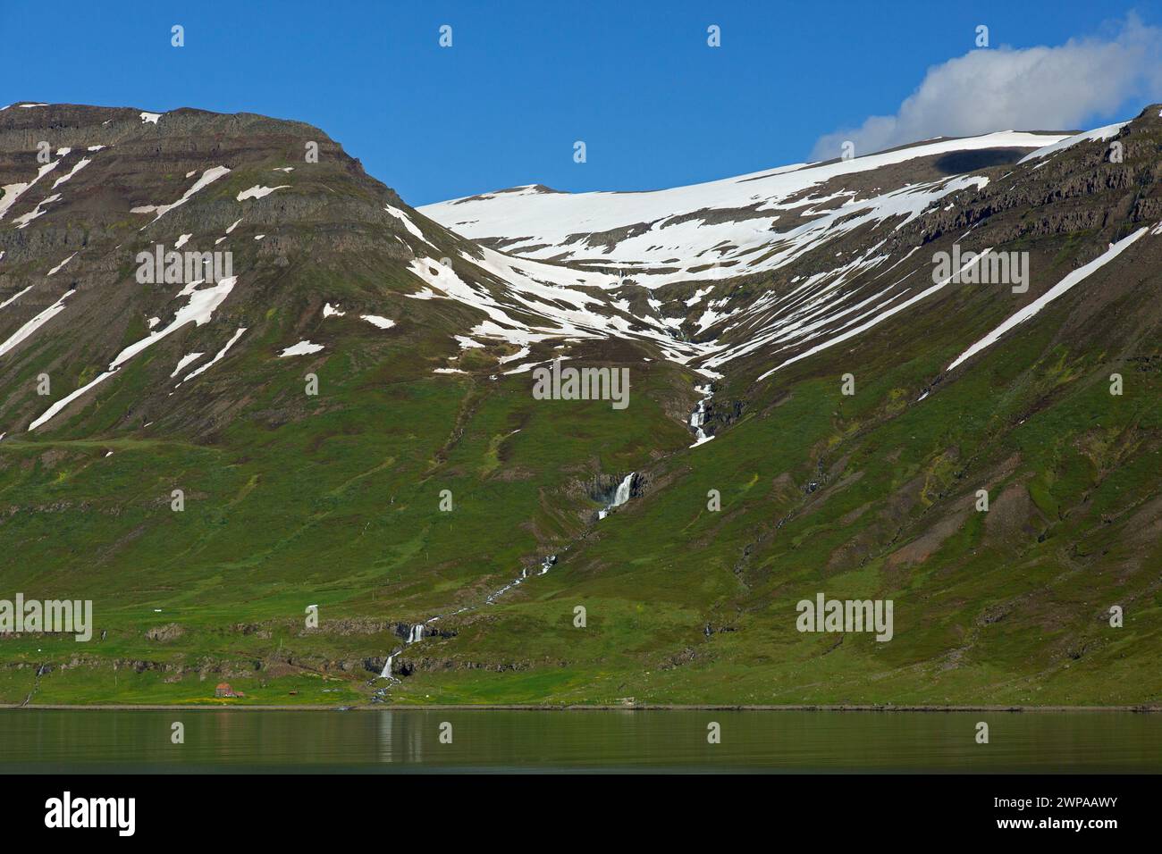Waterfall and desolate farm along the fjord Seyðisfjörður / Seydisfjoerdur in summer, Eastern Region / Austurland, Iceland Stock Photo