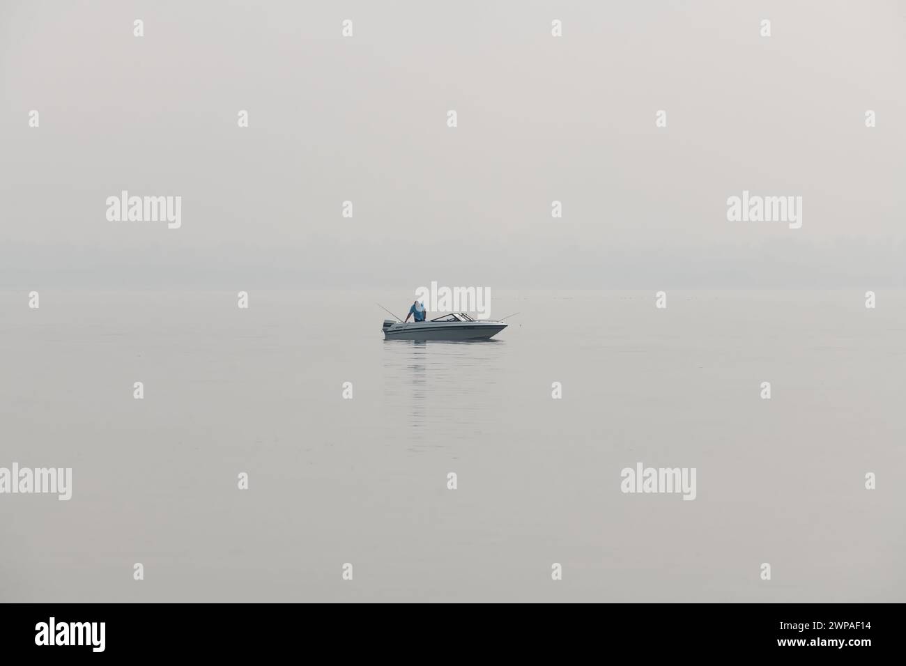 A fisherman on a boat in Lake Wabamun during poor visability due to forest fire smoke pollution in Alberta, Canada Stock Photo