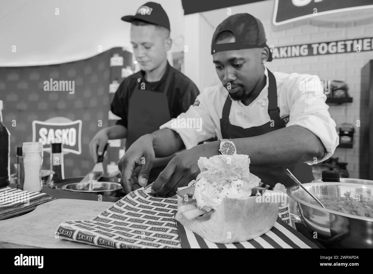 Two men in a kitchen making a big cake and mixing ingredients in a bowl Stock Photo