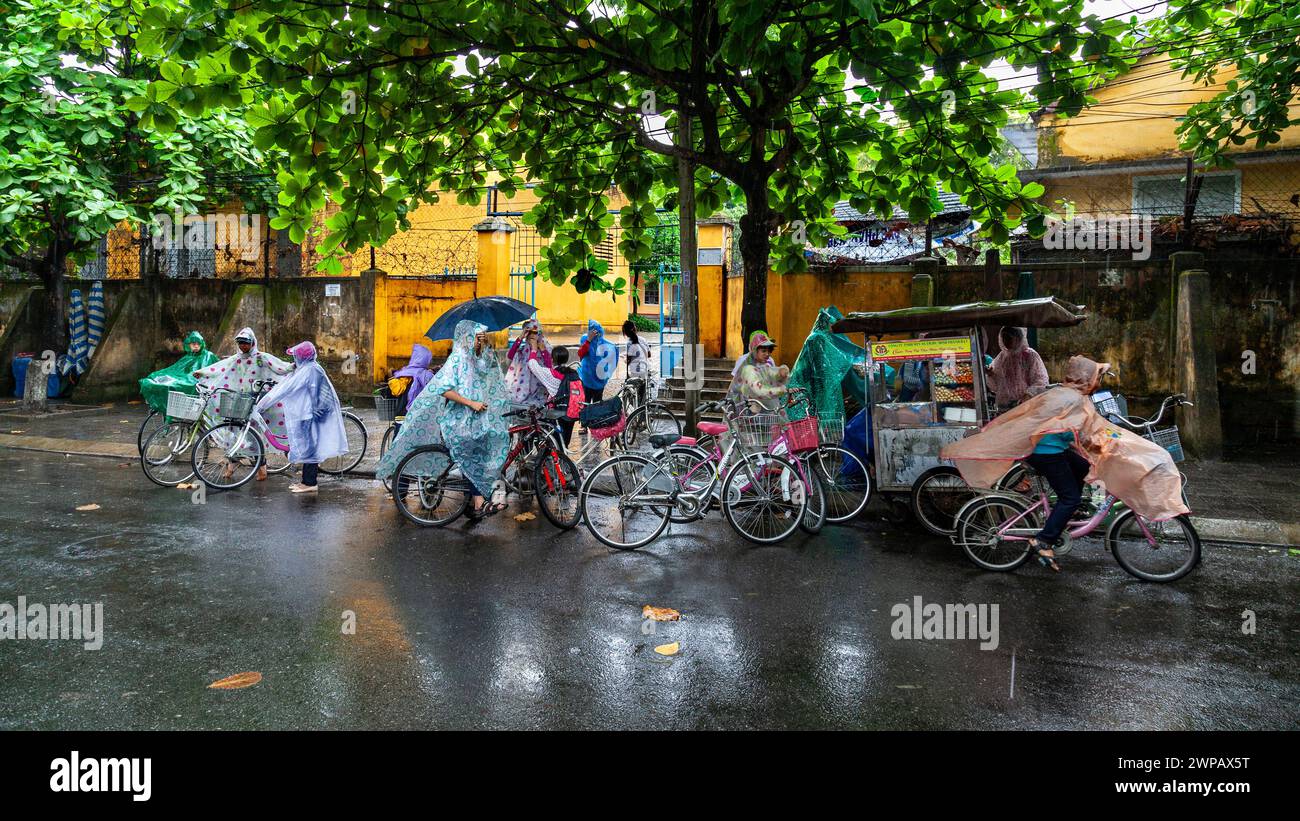 Hoi An, Vietnam; Street scene from the old town. Students finishing school, while rain is pouring down Stock Photo