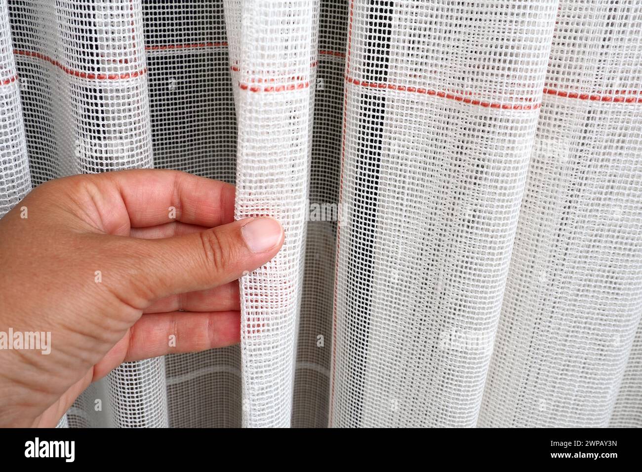 White coarse cotton or linen curtains made of weaves of thin threads. Simple compact economical apartment interior. Window decoration in the room. A Stock Photo